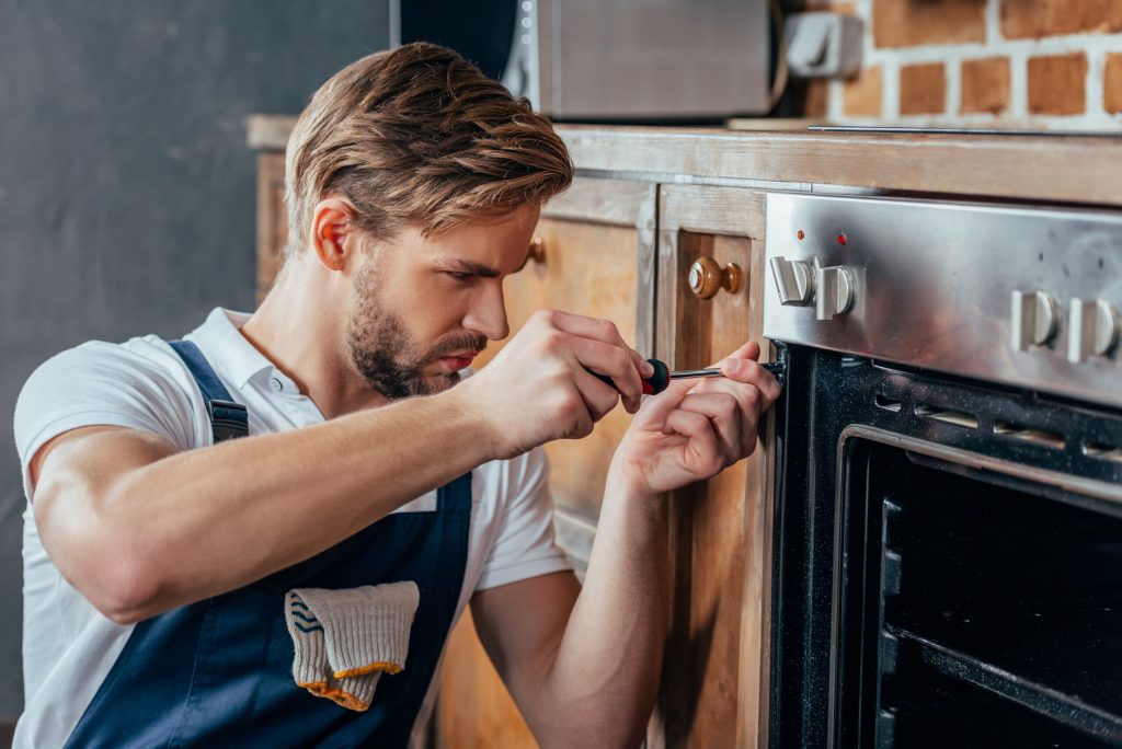 An applinace repairman is fixing an oven