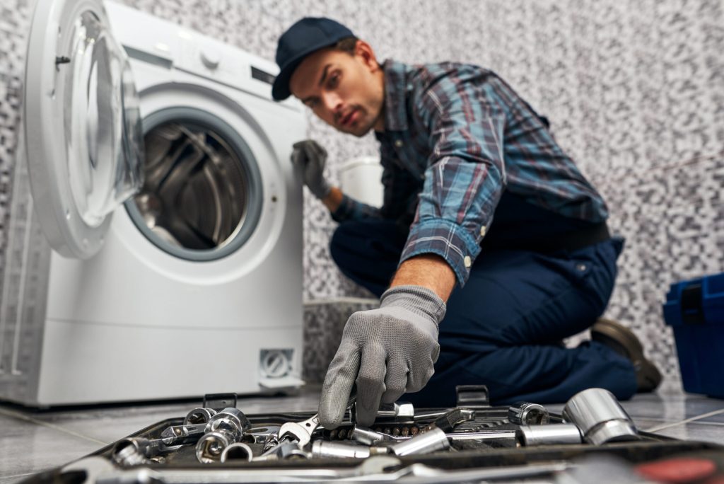 An appliance repair service man is grabbing a wrench to fix a dryer